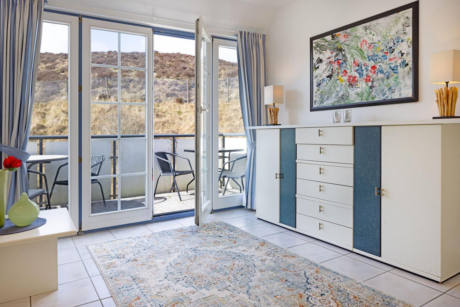 Raum mit Balkon, Schrank und Wandbild. Blick auf Hügellandschaft.