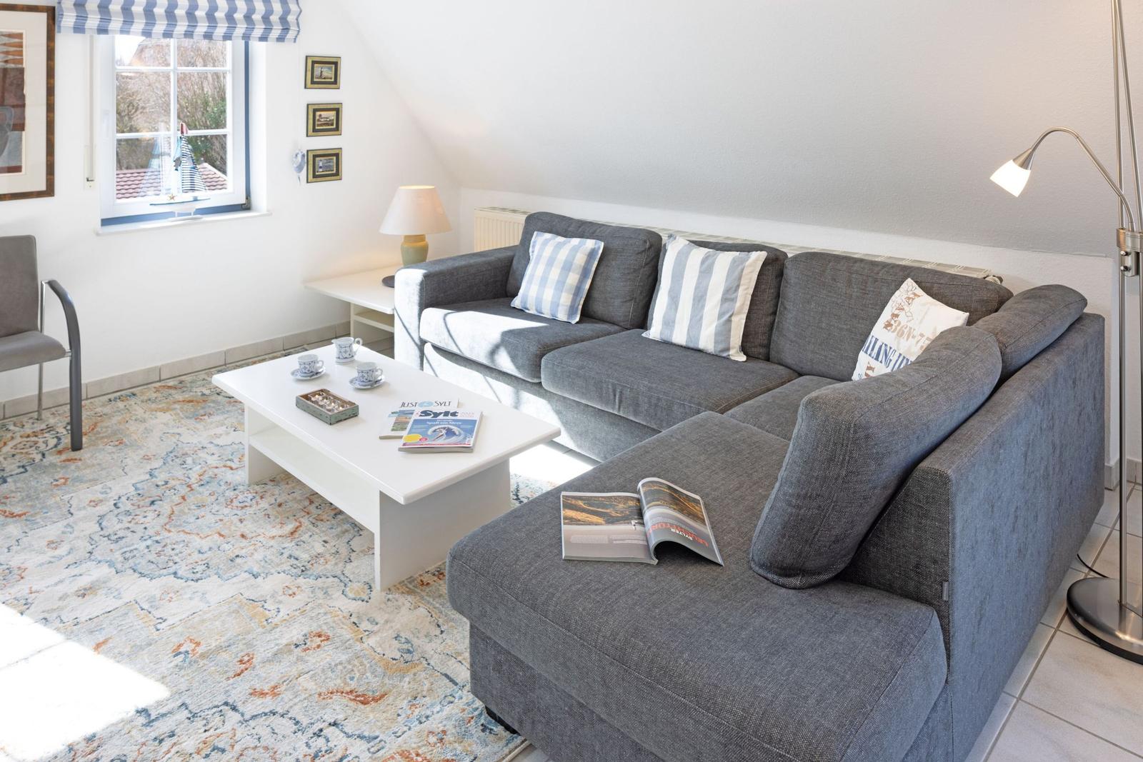 Ein Wohnzimmer mit grauem Sofa, weißem Couchtisch und gemustertem Teppich.