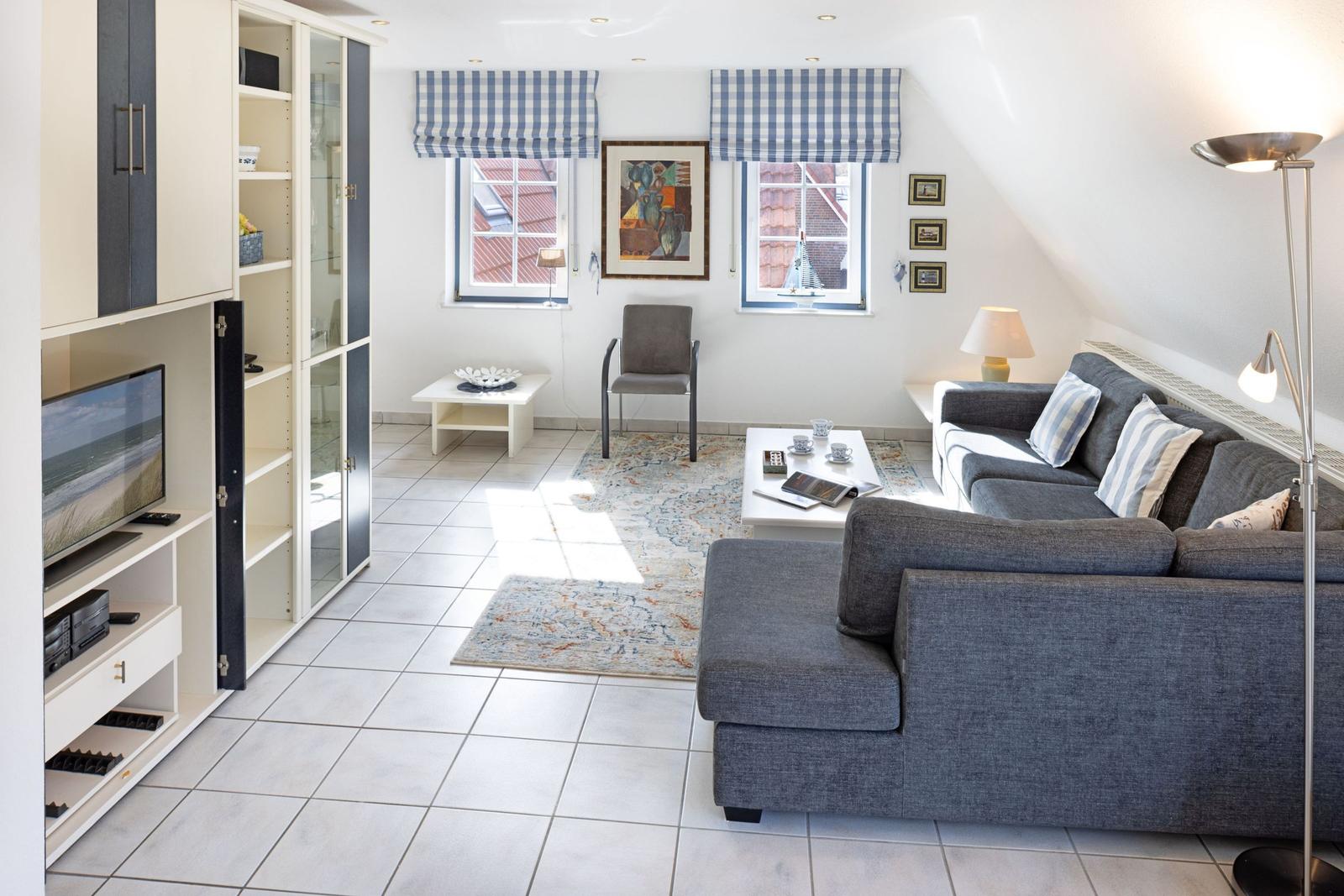 Wohnzimmer mit Sofa, TV, Fenstern und Bodenfliesen.