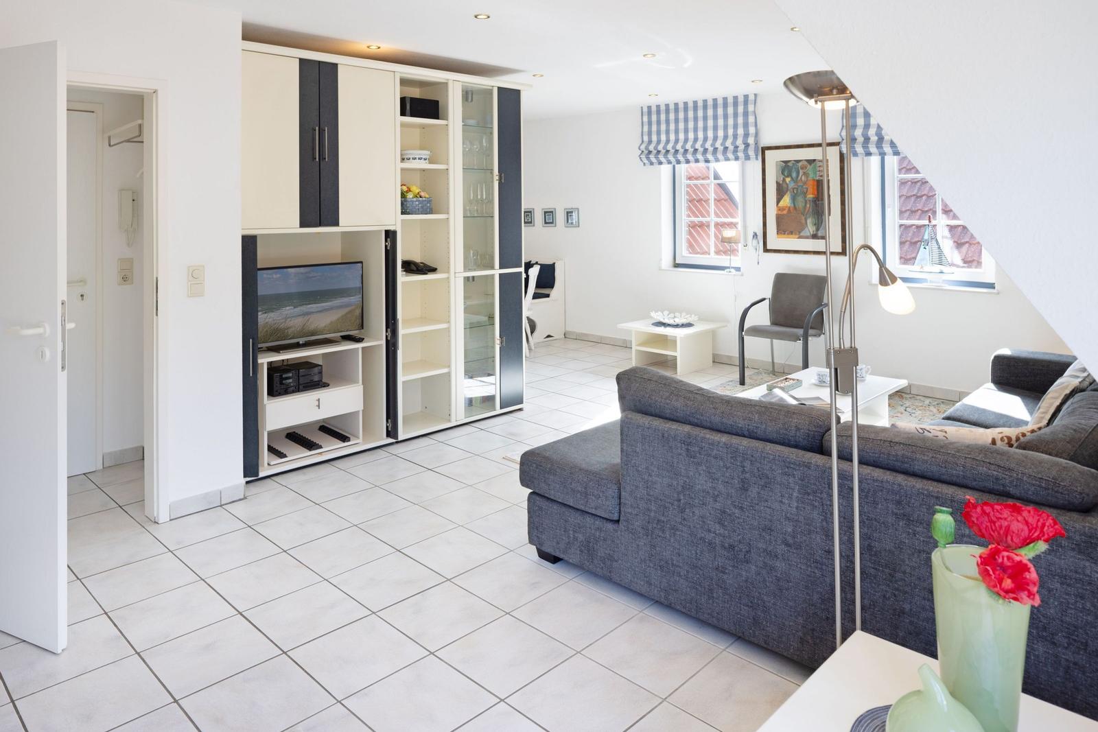 Wohnzimmer mit Sofa, TV-Möbel und Fenstern mit blau-weißen Rollläden.