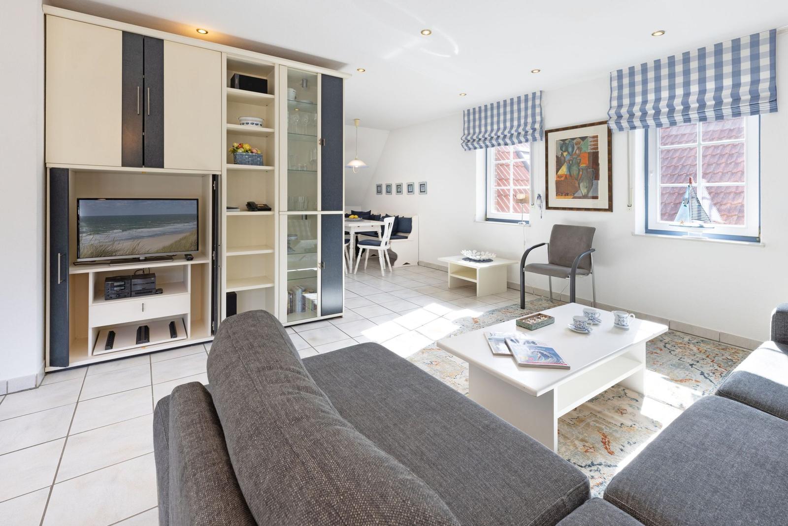 Wohn- und Essbereich mit Sofa, TV-Schrank und Fenstern mit blauen Rollläden.