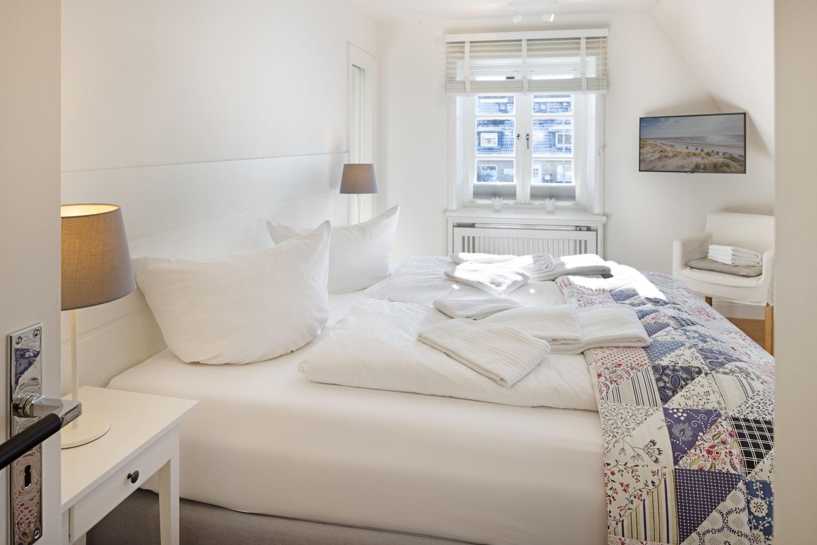 Schlafzimmer mit Bett, Fenster und Wandbild. Bett mit Decke und Kissen.