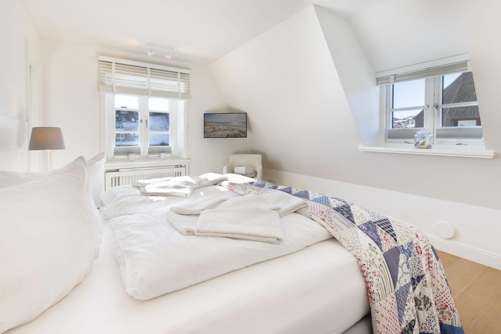 Schlafzimmer mit Dachfenster, Bett und TV. Fenster bieten Blick auf Dächer.