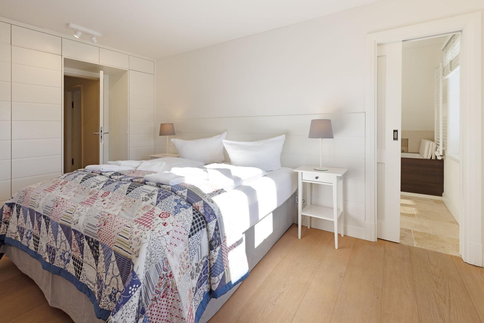 Schlafzimmer mit Bett, Nachttischen und integriertem Schrank. Tür führt in Bad.