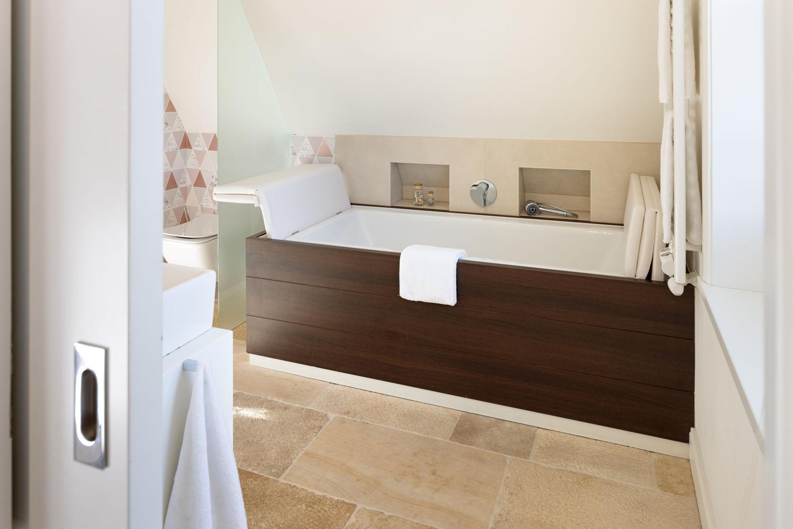 Bad mit Badewanne, Holzumrandung und Steinfliesenboden.