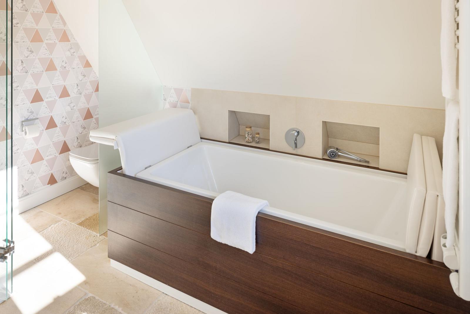 Bad mit Badewanne, Toilette und Glasdusche. Wand mit geometrischem Muster.