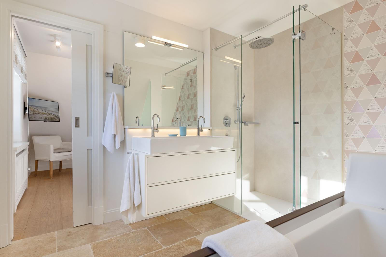 Badezimmer mit Dusche, Waschbecken und Badewanne. Durchgang in Schlafzimmer mit TV.