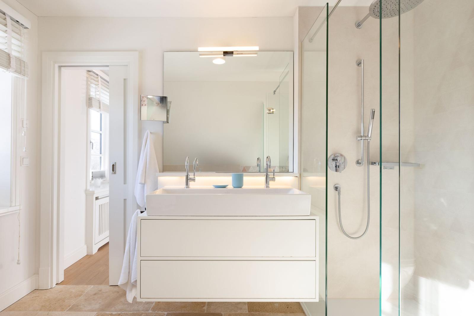 Badezimmer mit Dusche, Waschbecken und Spiegel. Holzfußboden und weiße Wände.