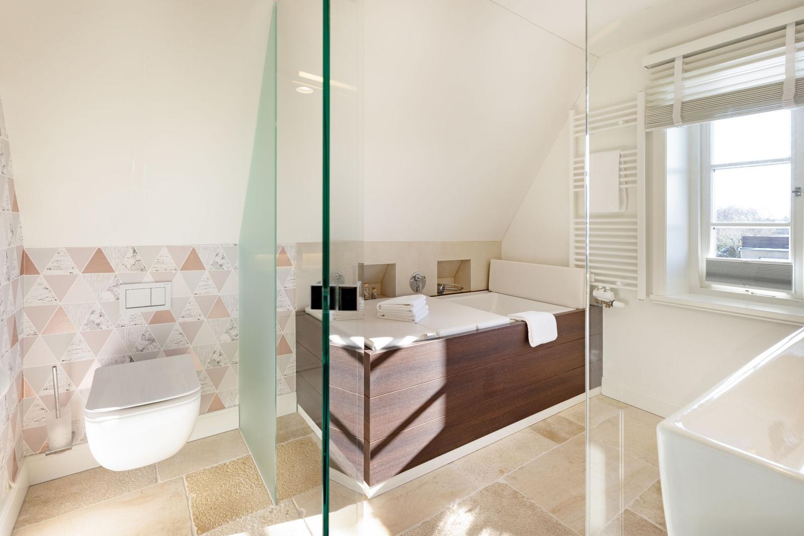 Badezimmer mit Badewanne, Toilette und Fenster. Wand mit Dreiecksmuster.