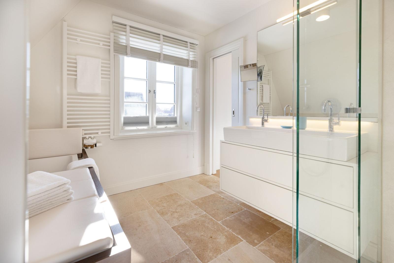 Badezimmer mit Dusche, Waschbecken und Fenster. Fliesenboden und Heizkörper.