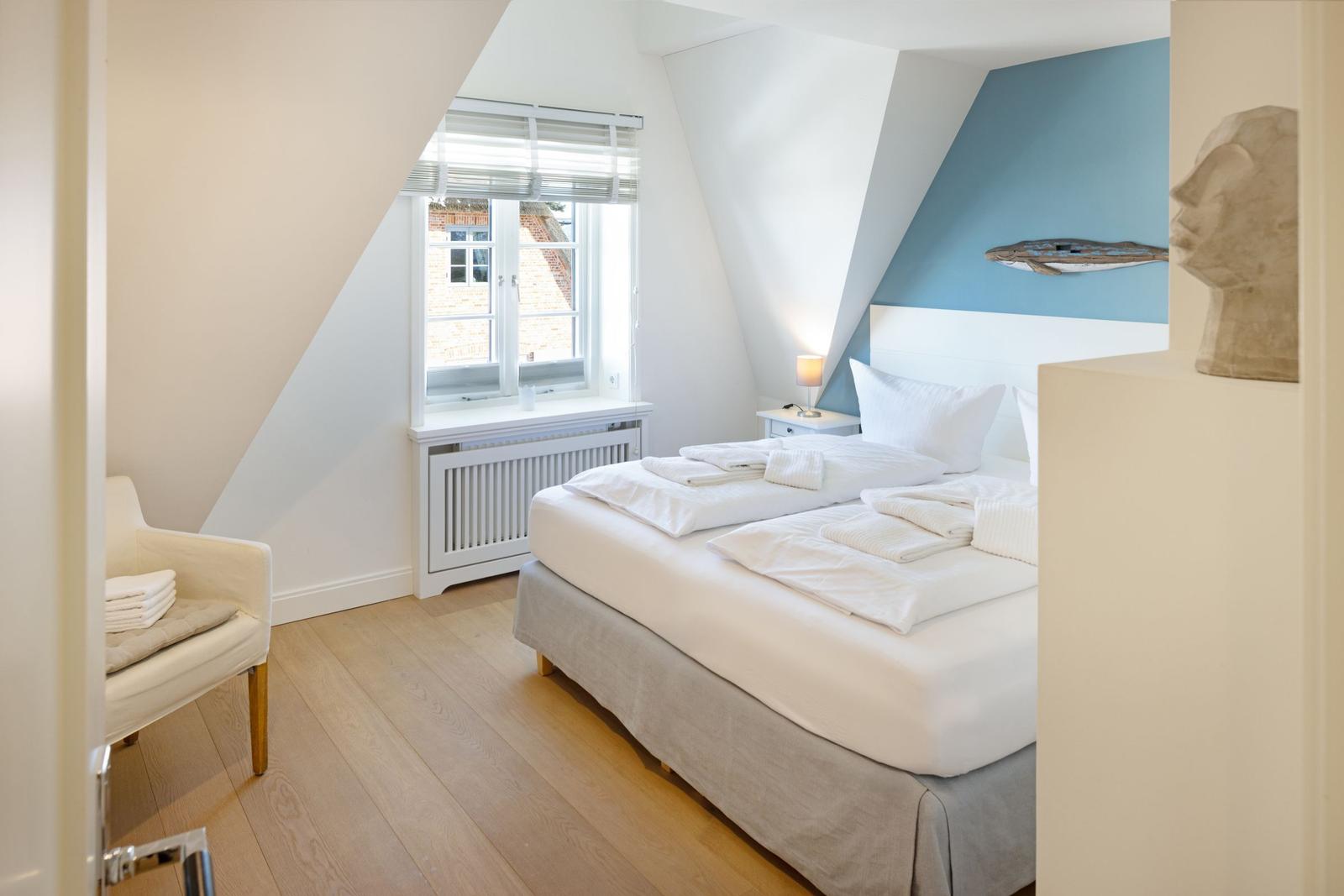 Schlafzimmer mit Dachbodenfenster, Bett und Sessel. Wand in Blau und Weiß.