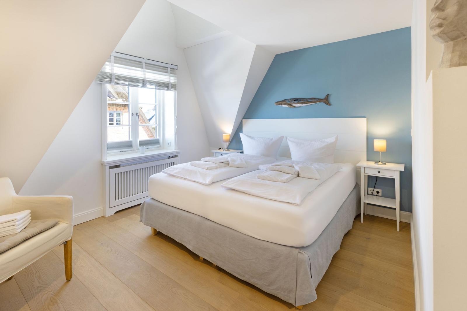 Schlafzimmer mit Doppelbett, blauer Wand und Fenster mit Blick nach draußen.