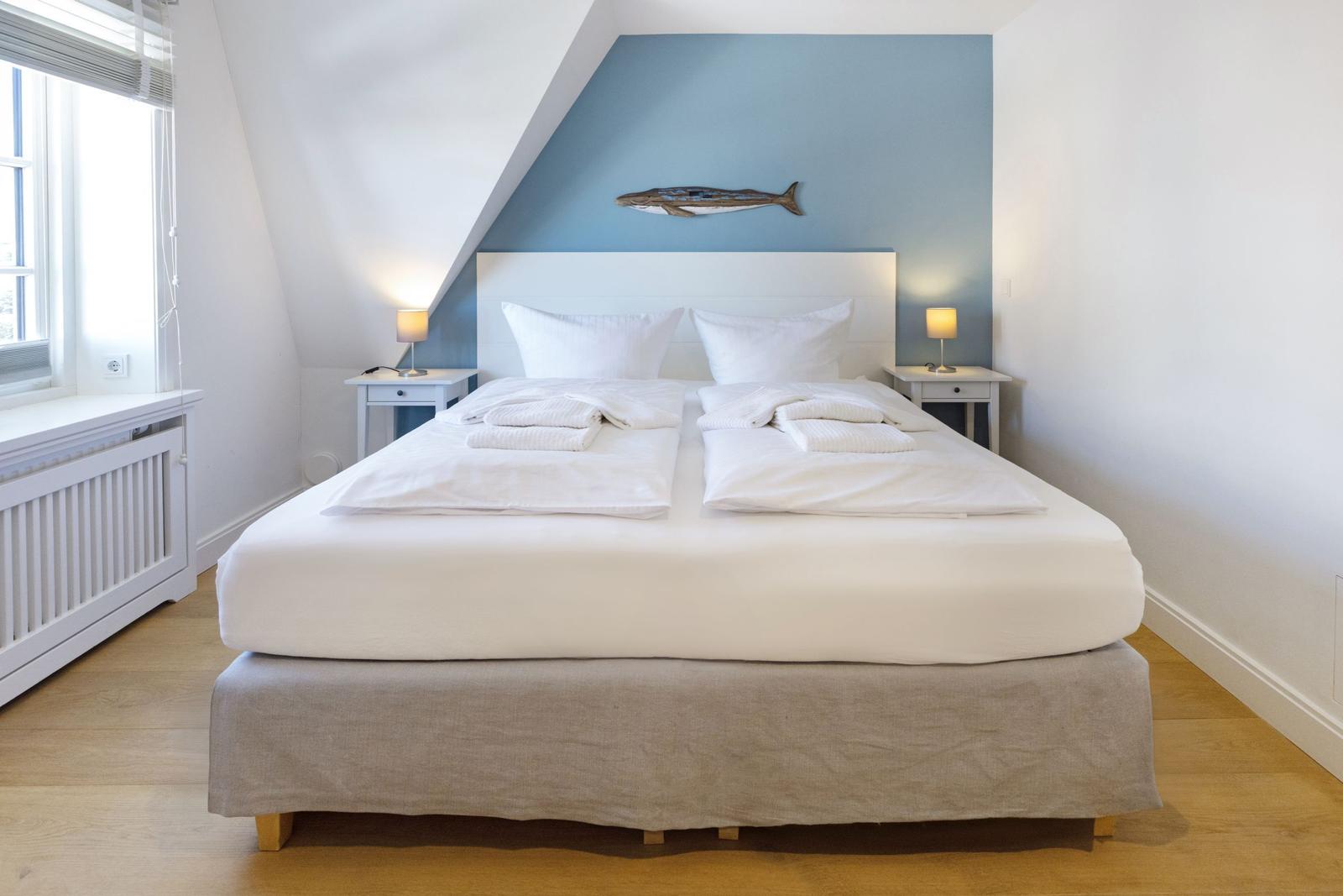 Doppelbett mit weißer Bettwäsche, zwei Nachttische und Wanddekoration.
