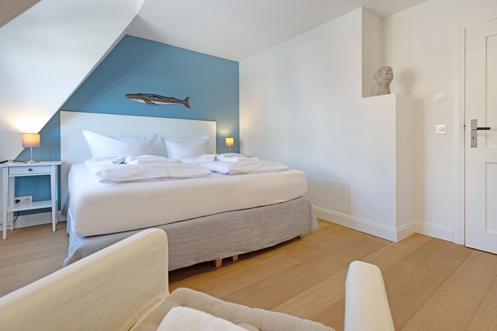 Schlafzimmer mit Doppelbett, blauer Wand und Holzboden. Dekoration mit Fisch und Skulptur.
