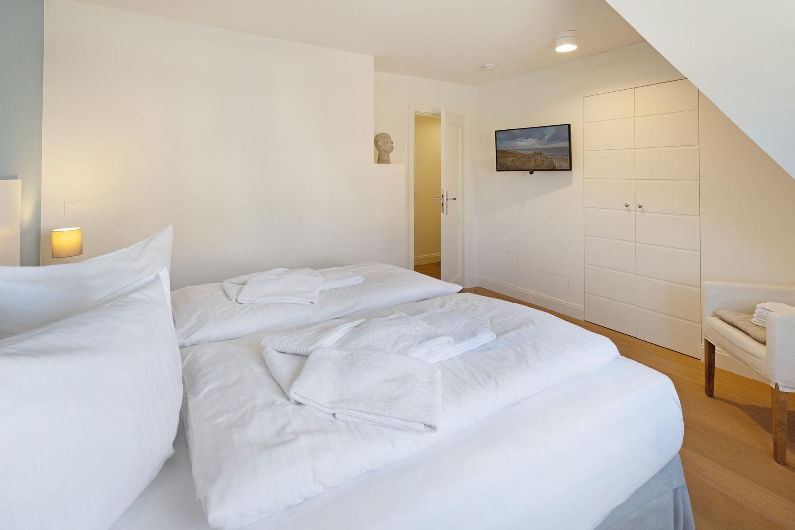Schlafzimmer mit Doppelbett, Kleiderschrank und Fernseher an der Wand.