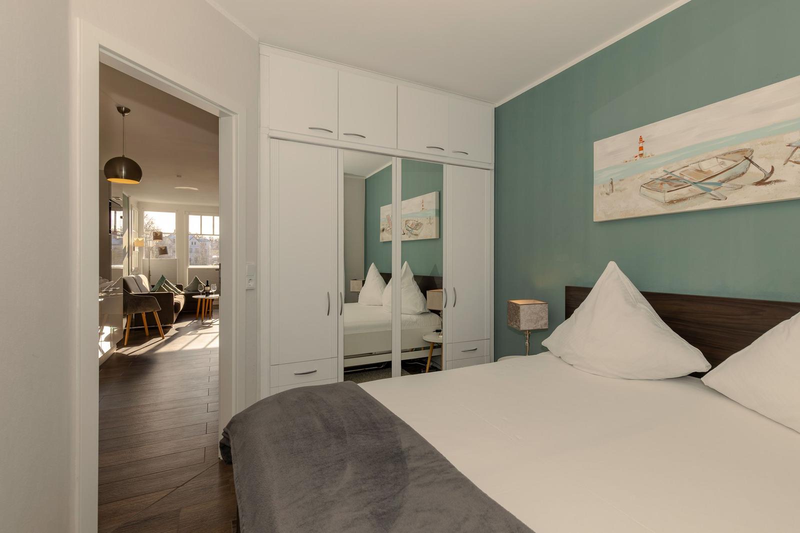 Schlafzimmer mit Bett, Kleiderschrank und Blick in Wohnbereich.