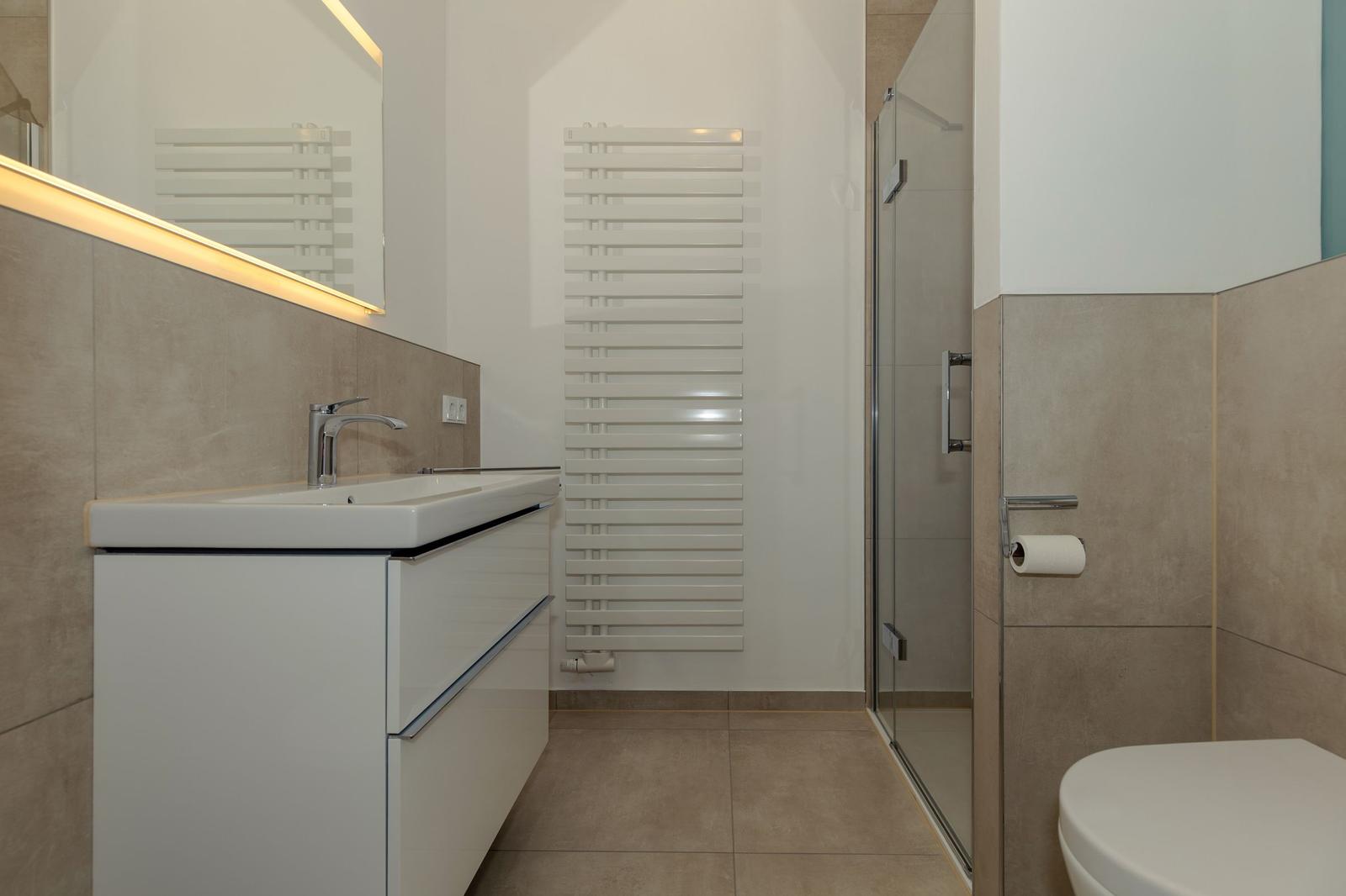 Badezimmer mit Waschbecken, Dusche und Toilette. Weiße Einbauschränke und Heizung.