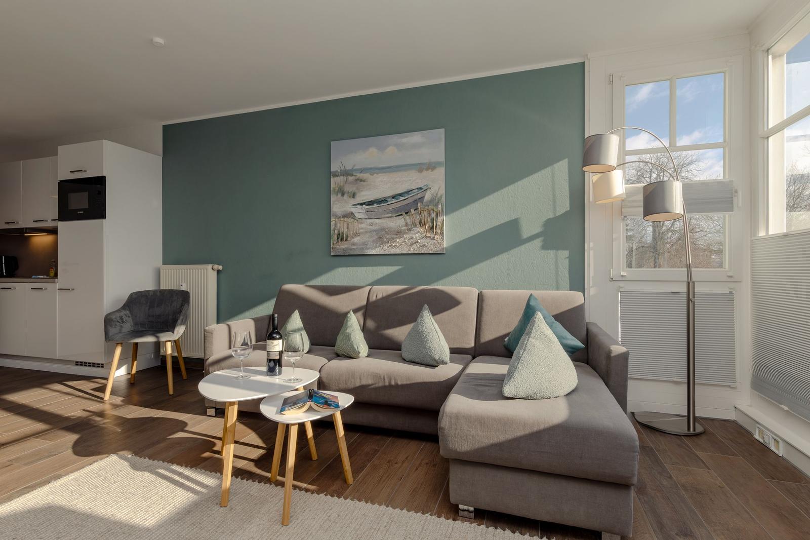 Wohnbereich mit Sofa, Tisch und Wandbild. Küche im Hintergrund.