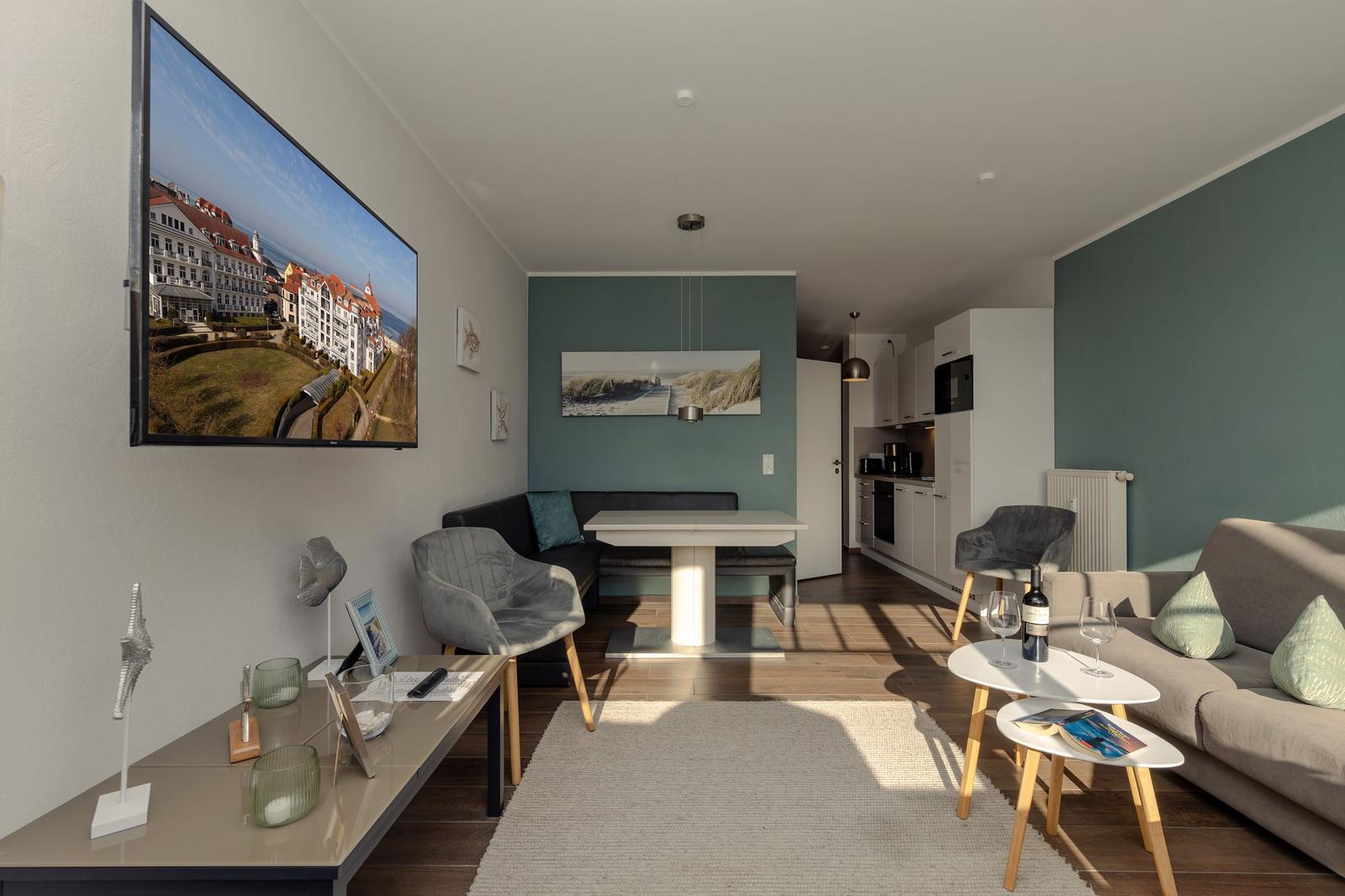 Wohn- und Essbereich mit TV, Sofa und Küchenbereich im Hintergrund.