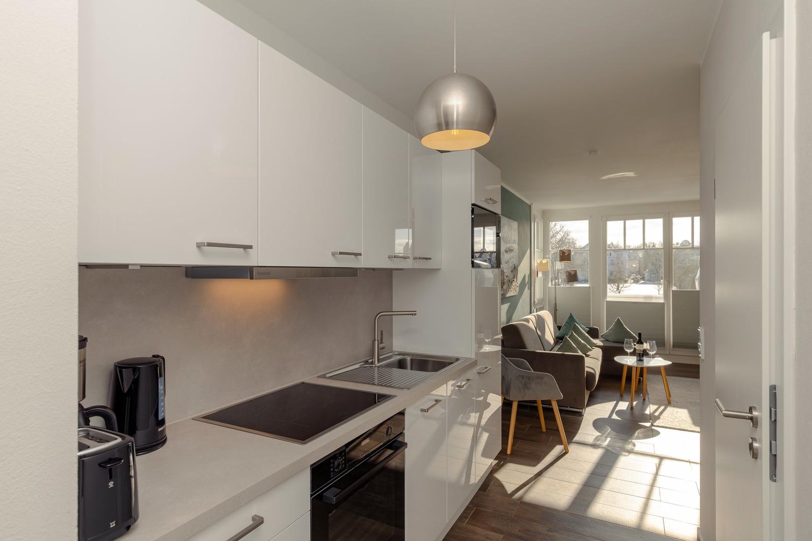 Küche mit weißen Schränken und modernem Design. Wohnbereich mit Sofa und Tisch.