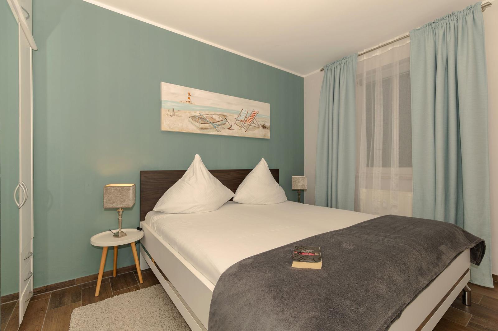 Schlafzimmer mit Bett, Nachttisch, Gardinen und Wandbild.