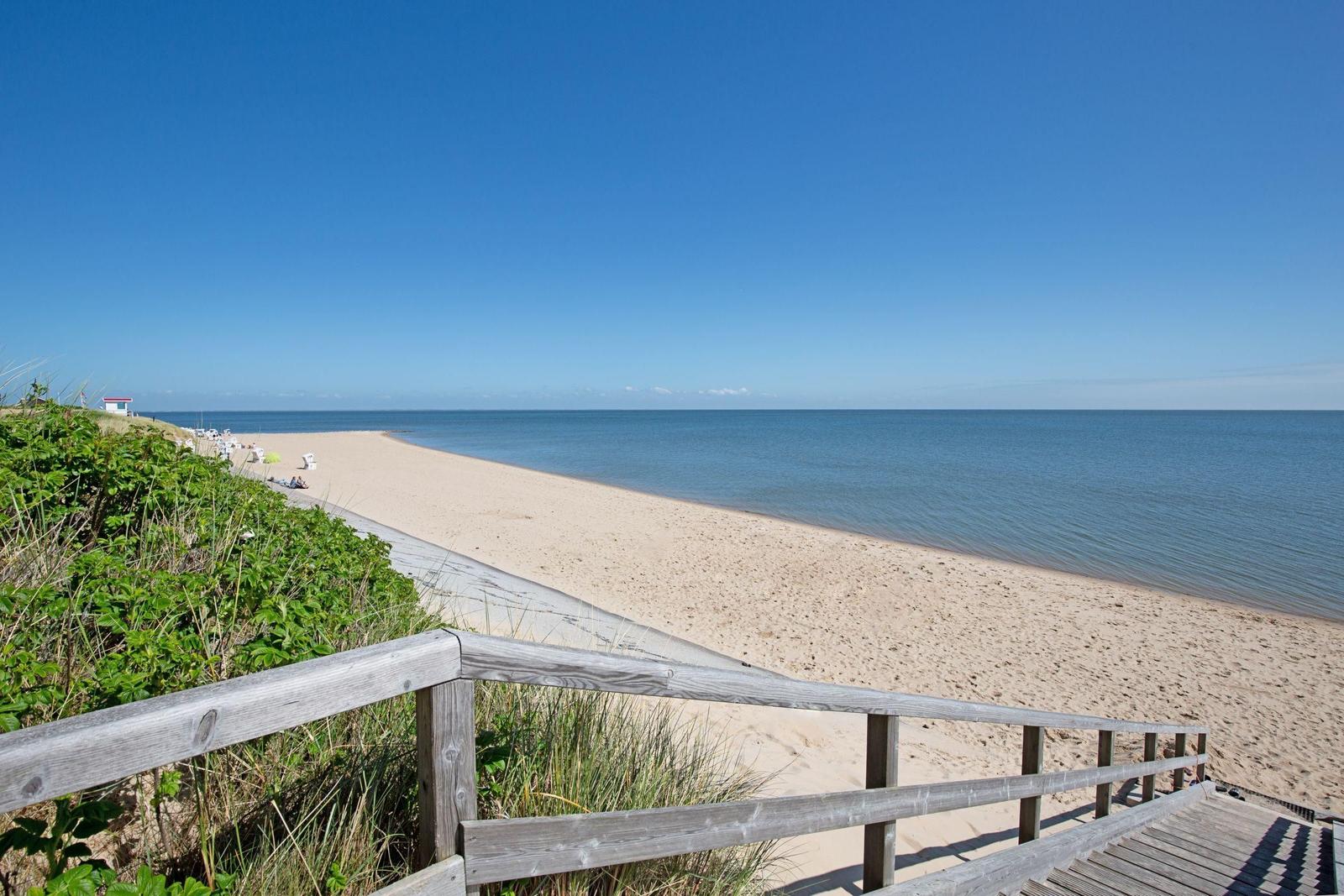 Holzsteg führt zum Strand. Sandstrand mit Meer und blauem Himmel.