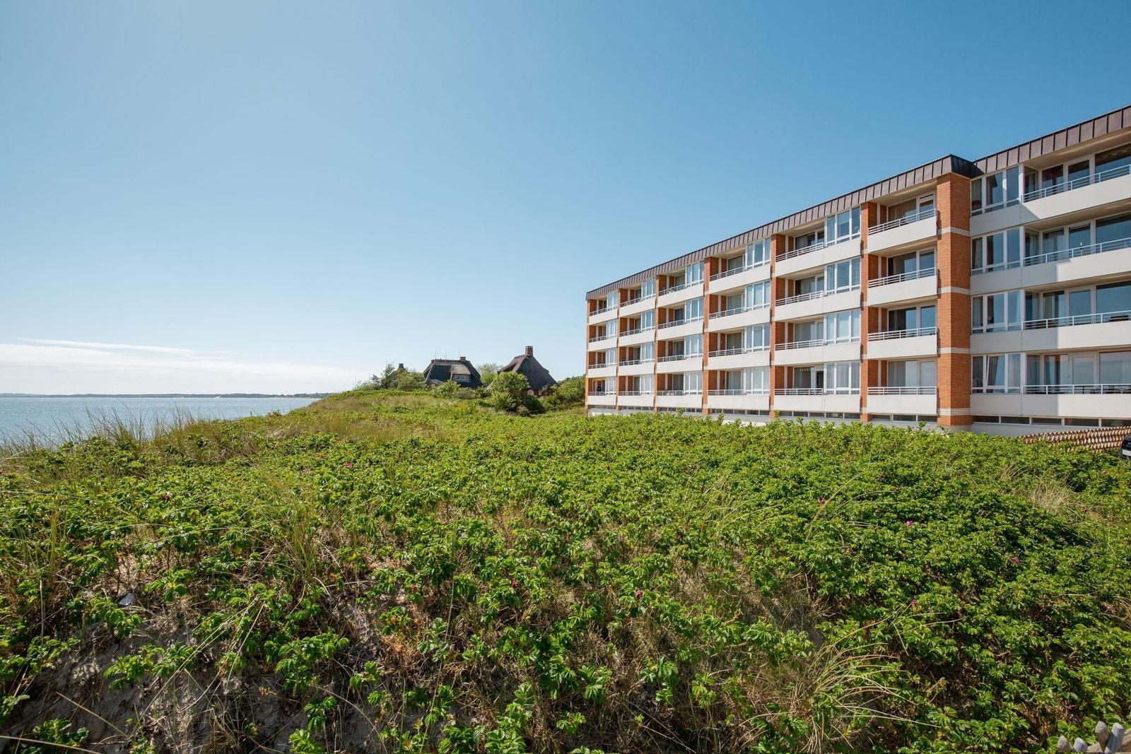 Modernes Mehrfamilienhaus am Ufer mit Blick auf das Wasser und grüne Dünen.