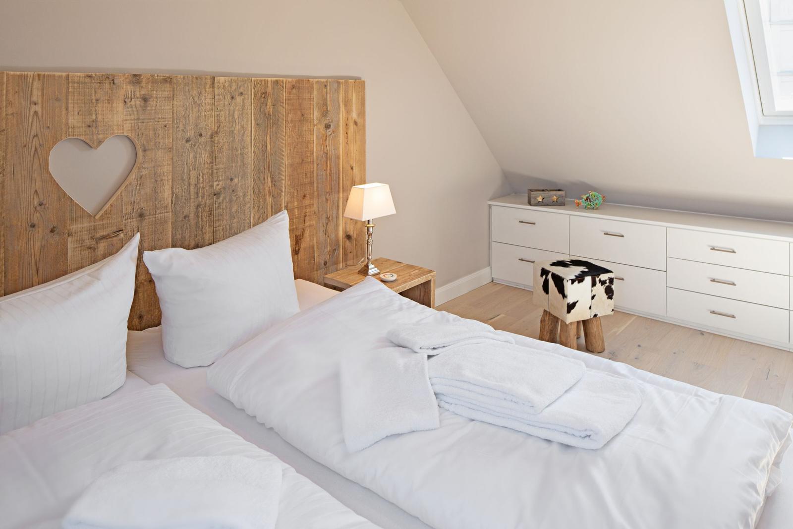Schlafzimmer mit Holzbett, Nachttisch und Schrank. Fenster und Holzboden sichtbar.