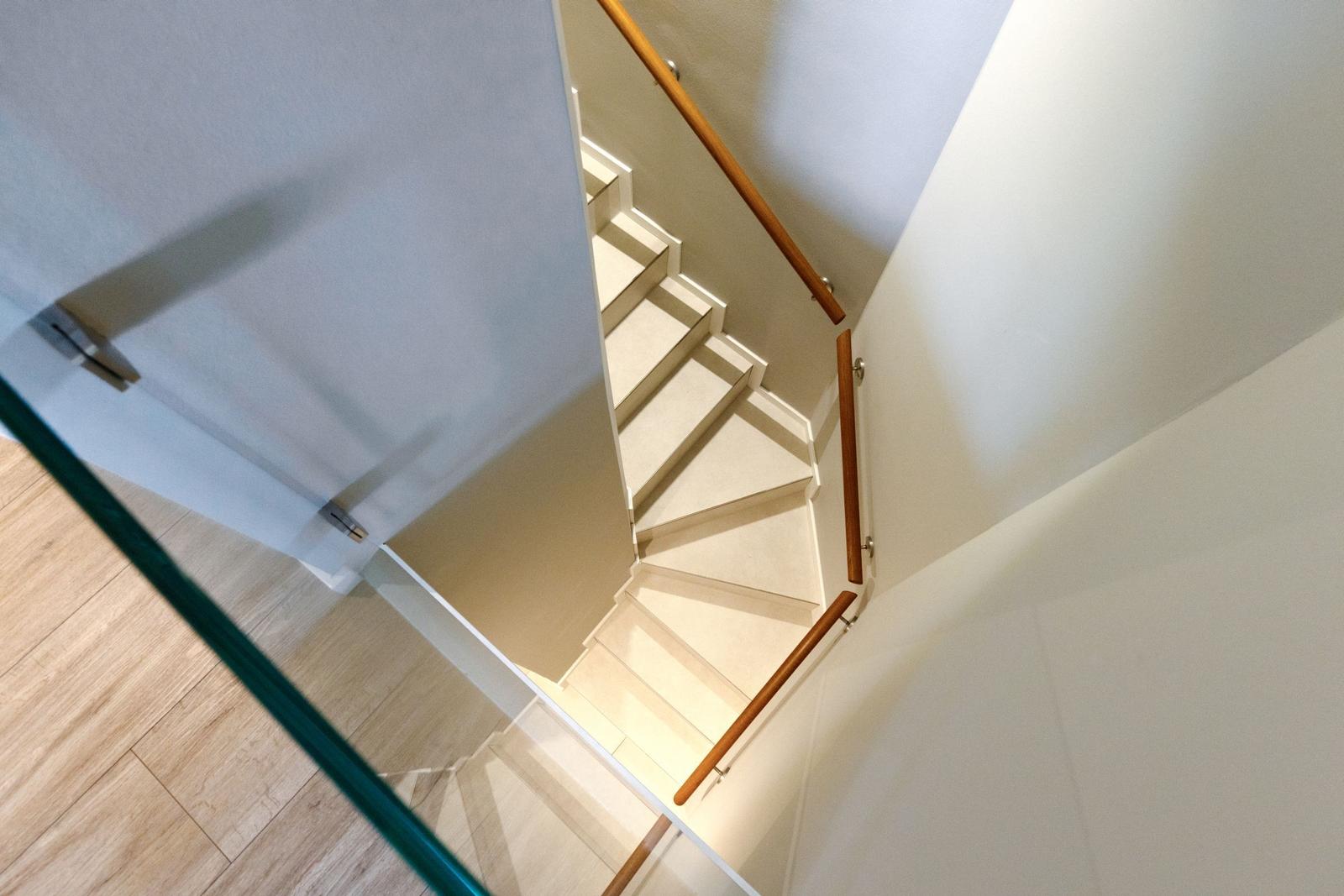 Helle Treppe mit Holzgeländer und Glasbrüstung führt in den Obergeschossbereich.