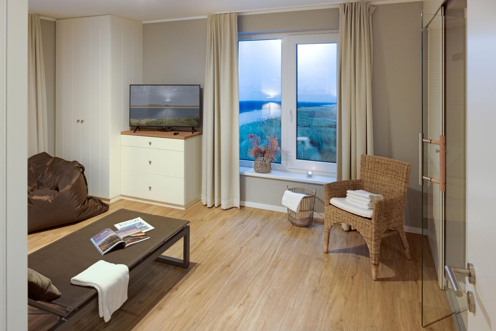 Wohnraum mit TV, Sitzgelegenheiten und Blick auf die Küste.
