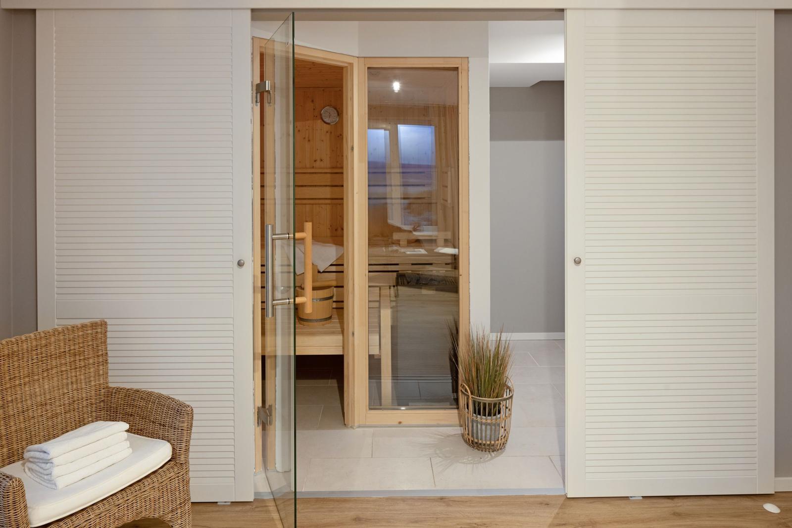 Sauna mit Glasfront und Holzbank. Außerhalb Wickerstuhl mit Handtuch.