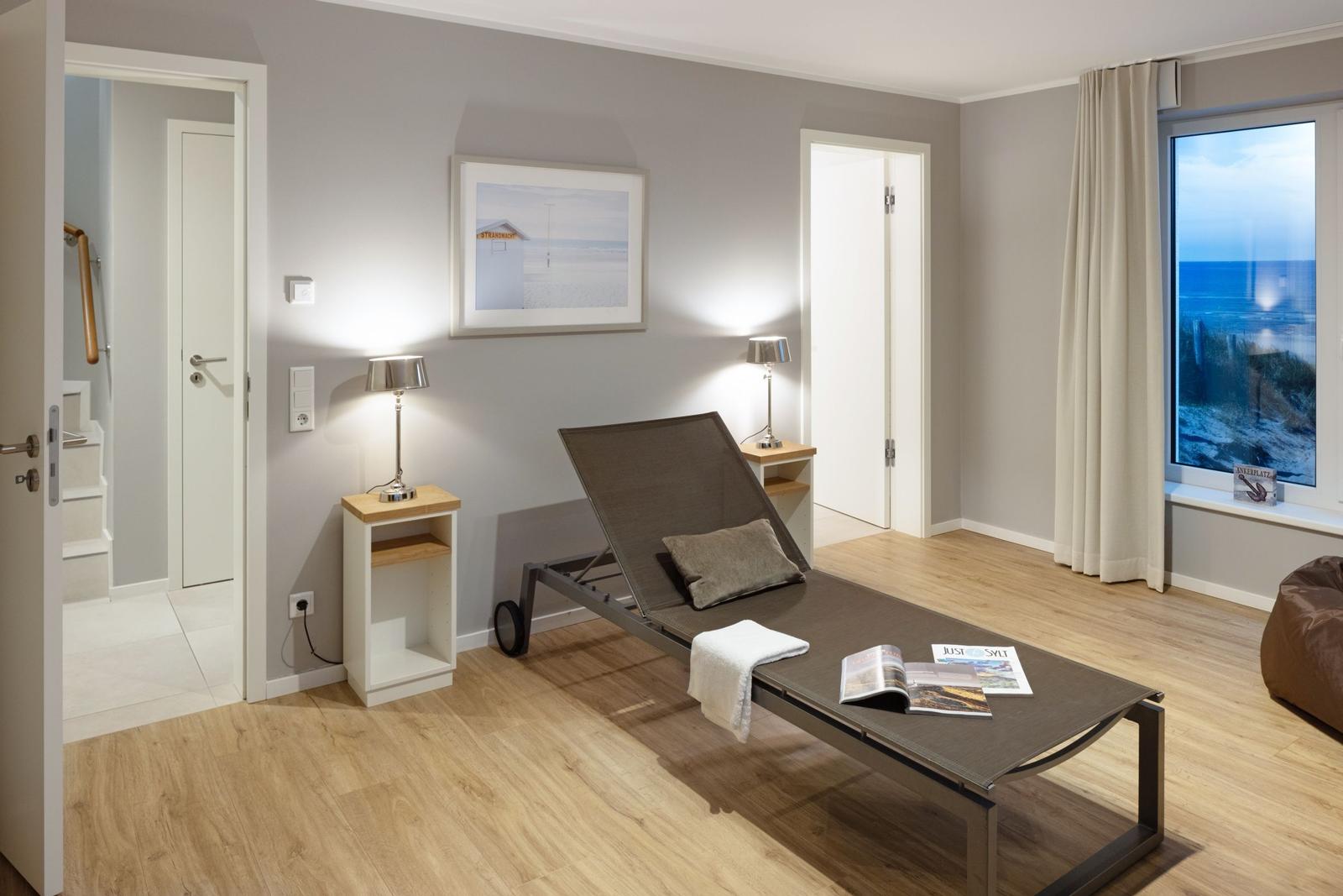 Zimmer mit Liege, Fensterblick aufs Meer und zwei Nachttische mit Lampen.