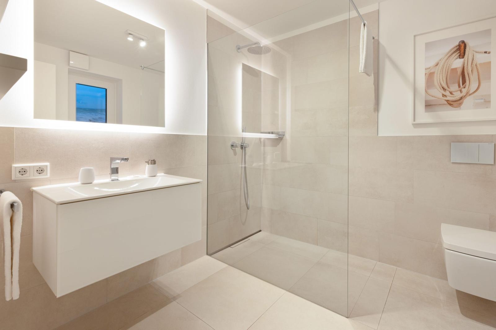 Moderne Badezimmer mit Dusche, Waschbecken und Toilette. Spiegel zeigt Blick auf Meer.