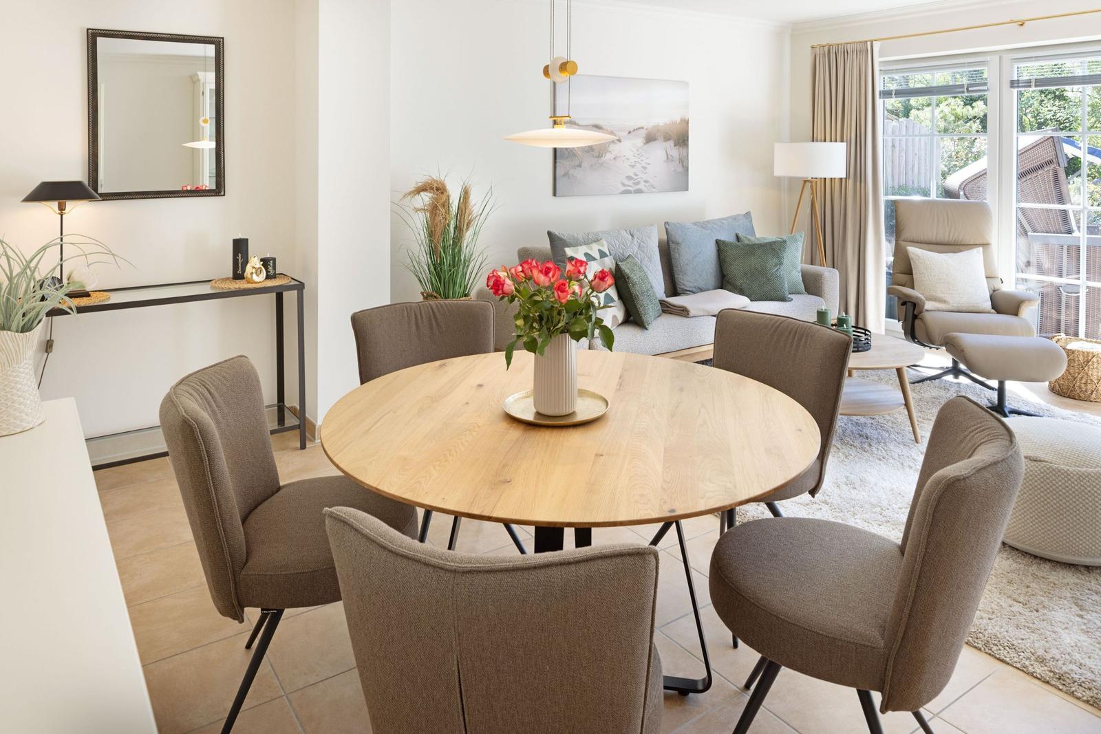 Runder Esstisch mit Stühlen und Blumen in Wohnzimmer mit Sofa und Sitzgelegenheit.