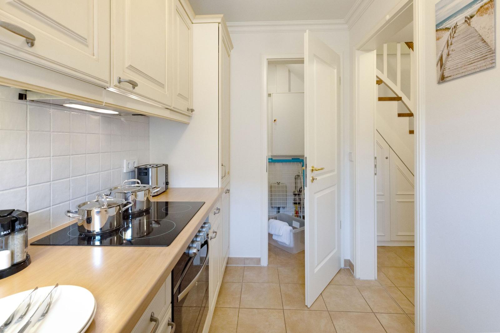 Küche mit Arbeitsfläche, Herd und Küchenschränken. Hinterher ist eine Treppe und ein Raum mit Waschbecken.