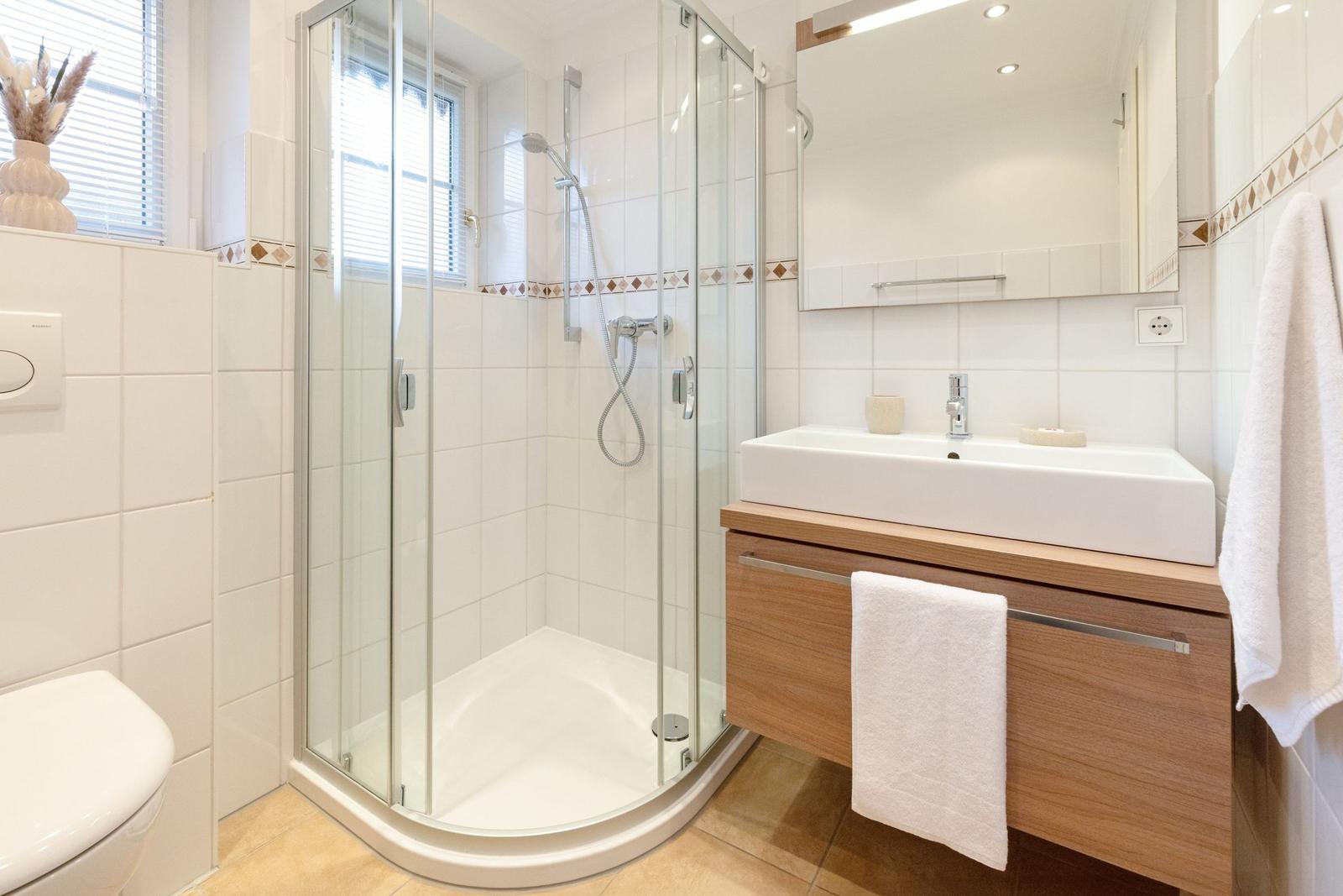 Badezimmer mit Dusche, Waschbecken und Toilette. Holzunterschrank und Spiegel.