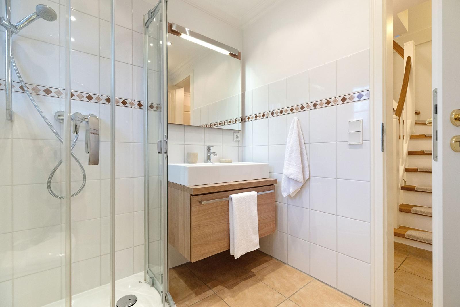 Badezimmer mit Dusche, Waschbecken und Spiegel. Fliesenwand mit Mosaikstreifen.
