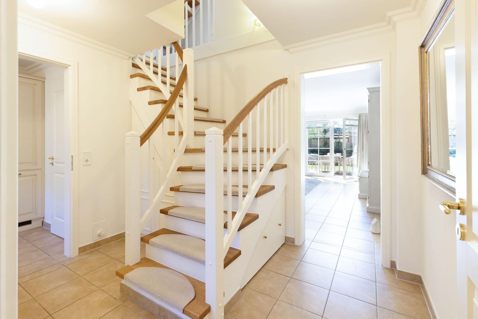 Haus mit Holztreppe und weißen Geländern. Durchgang zu Wohnbereich und Terrasse.