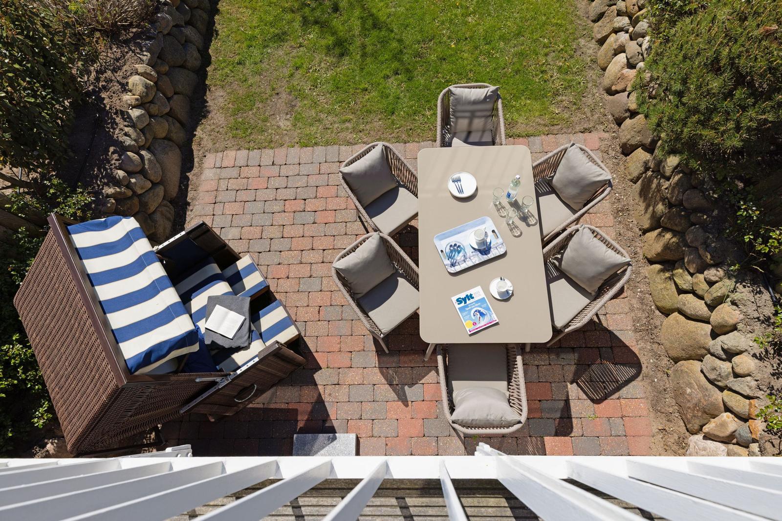 Terrasse mit Tisch, sechs Stühlen und Liegestuhl mit blau-weißem Gestell.