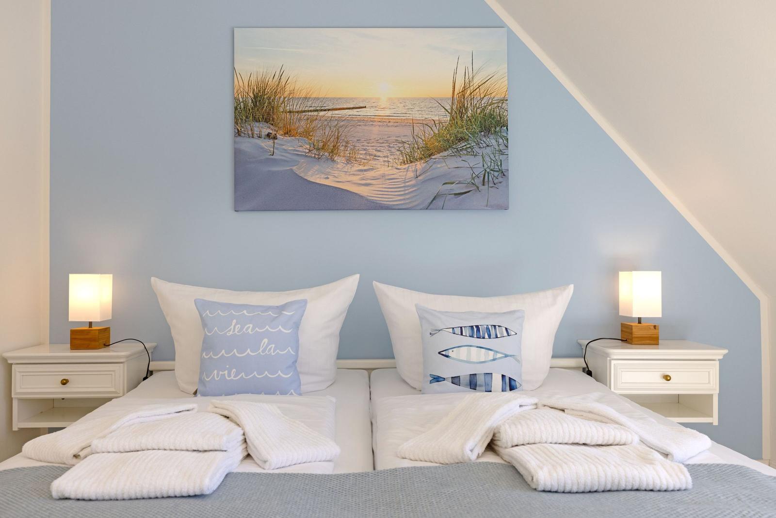 Zwei Betten mit weißen Kissen und Decken unter einem Wandbild mit Strandmotiv.