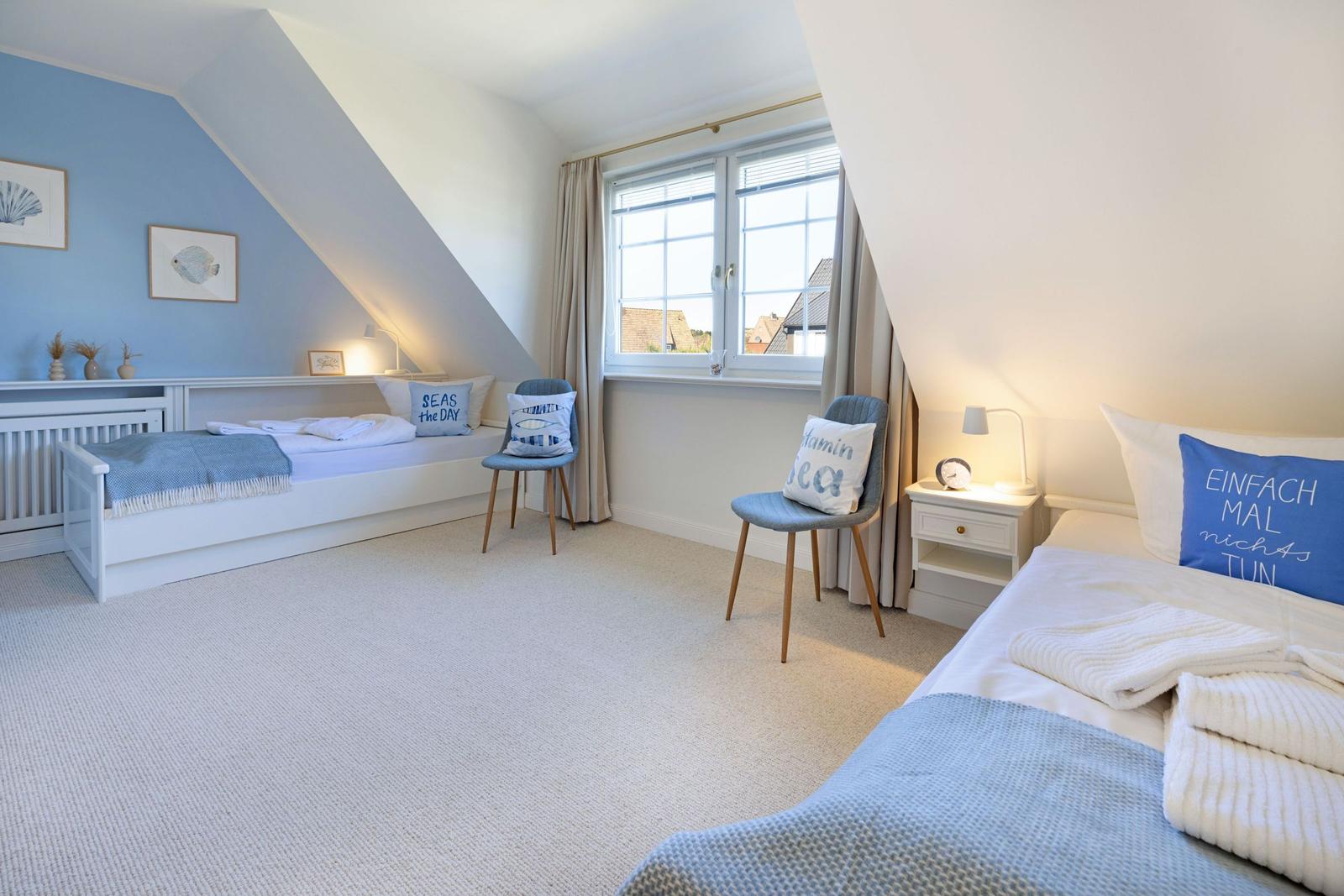 Zimmer mit zwei Betten, Fenster, Stühlen und blauen Kissen.