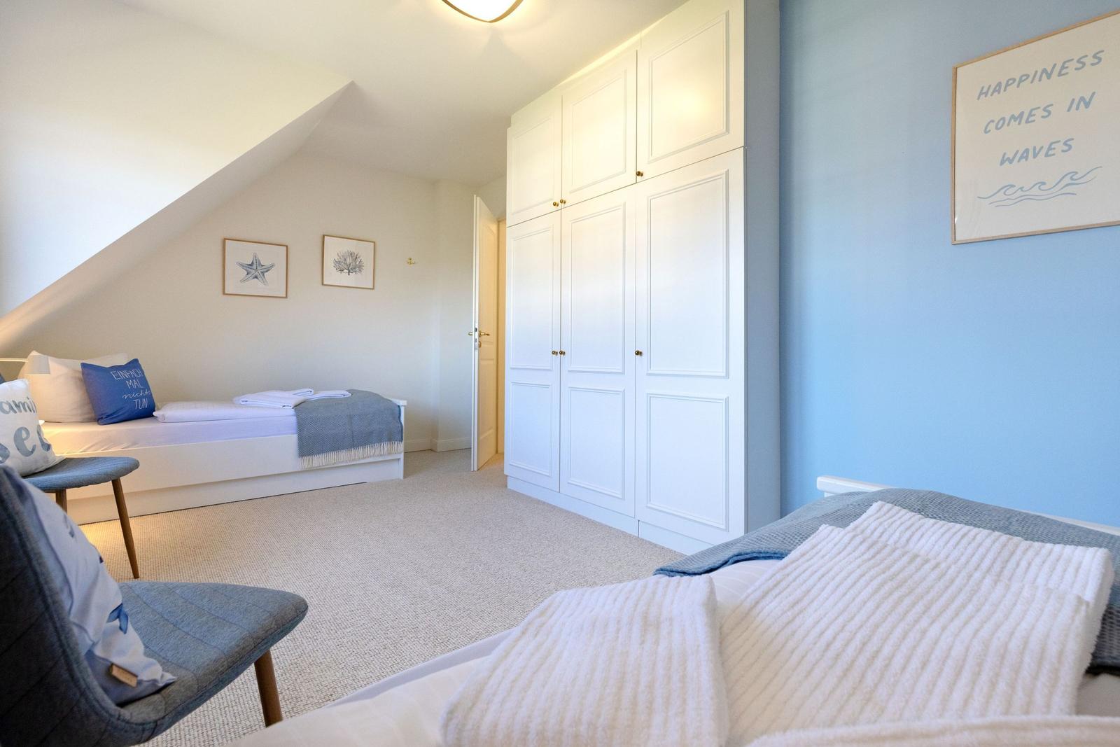 Schlafzimmer mit zwei Betten, weißen Schränken und blauen Wänden. Wandbild mit Wellenmotiv.