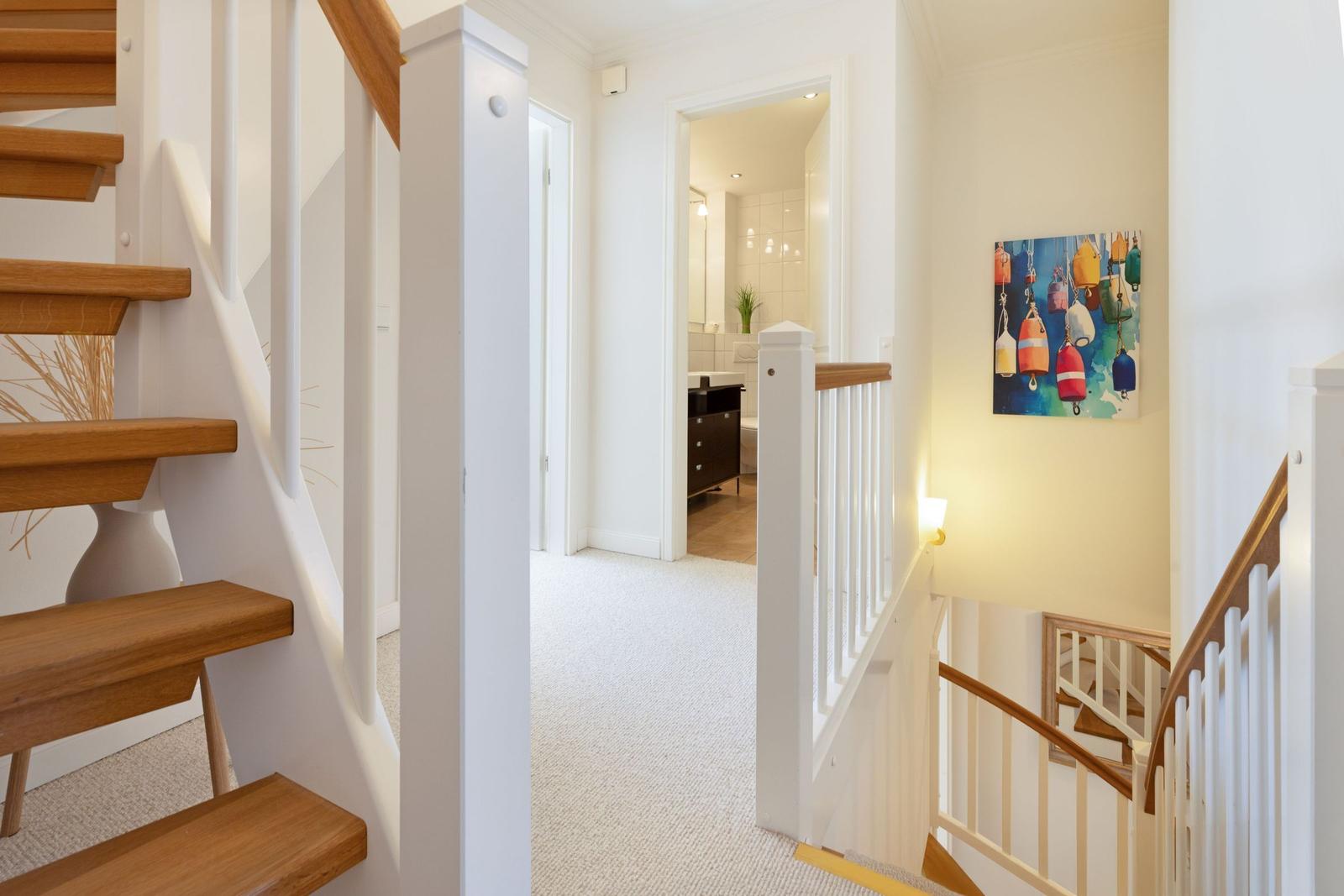 Hausflur mit Holztreppe und Bild an der Wand. Blick in das Bad.
