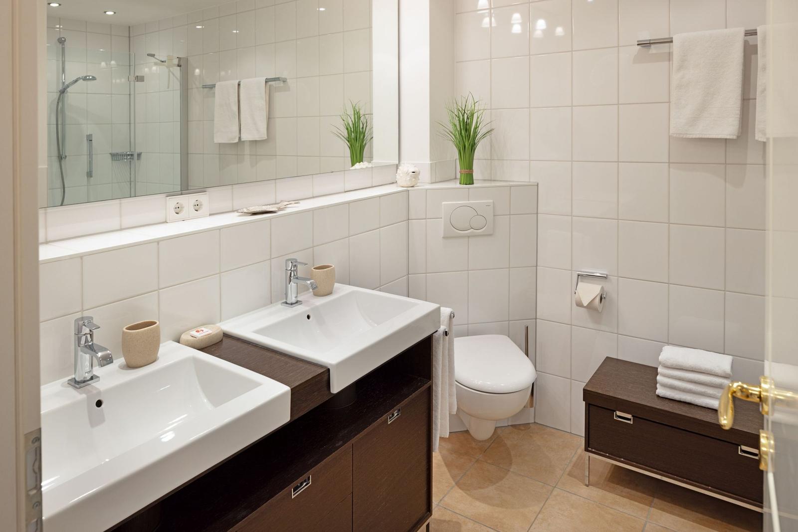 Badezimmer mit zwei Waschbecken, Toilette, Dusche und Holzregal.
