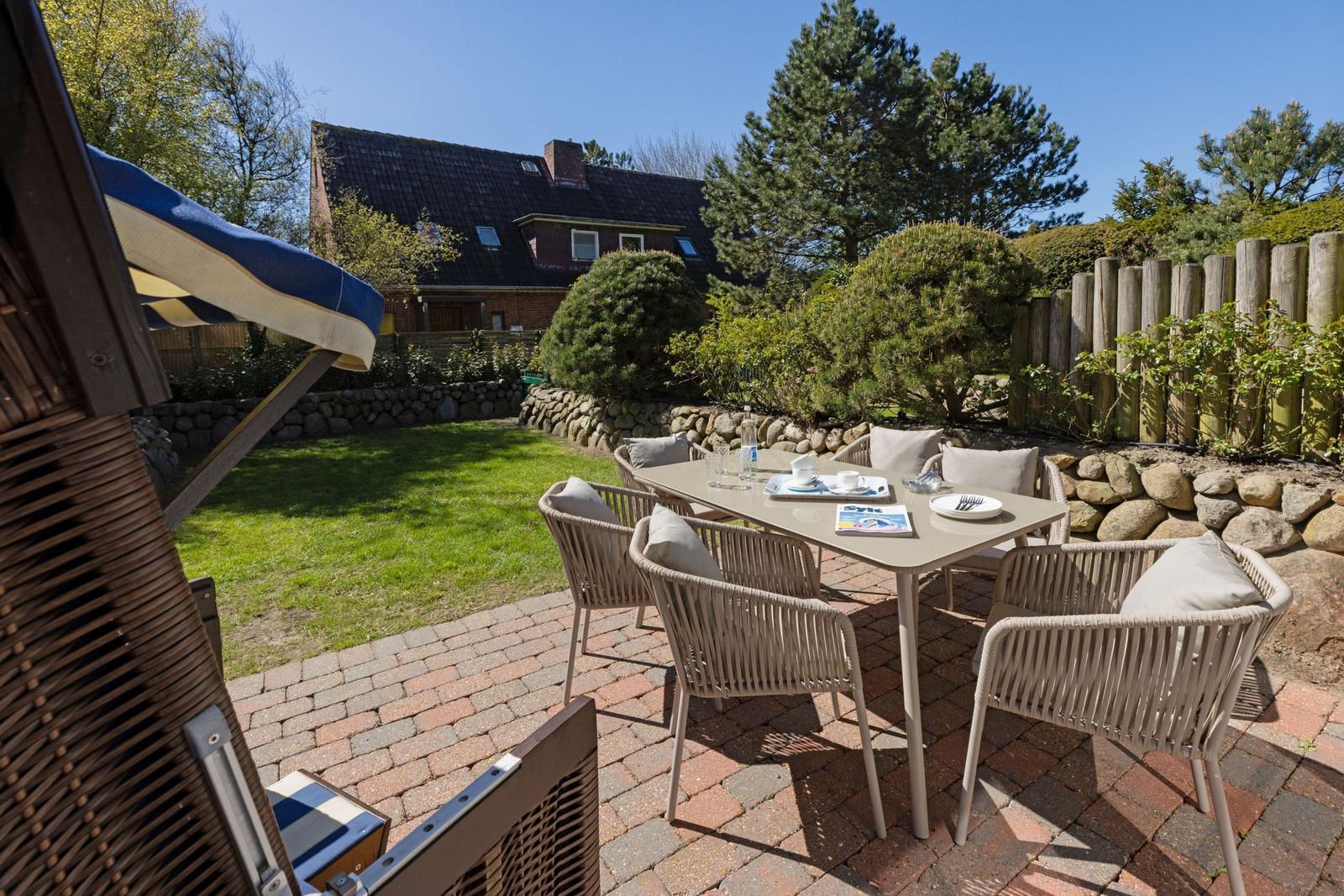 Terrasse mit Tisch und Stühlen, Grünfläche und Holzzaun im Hintergrund.