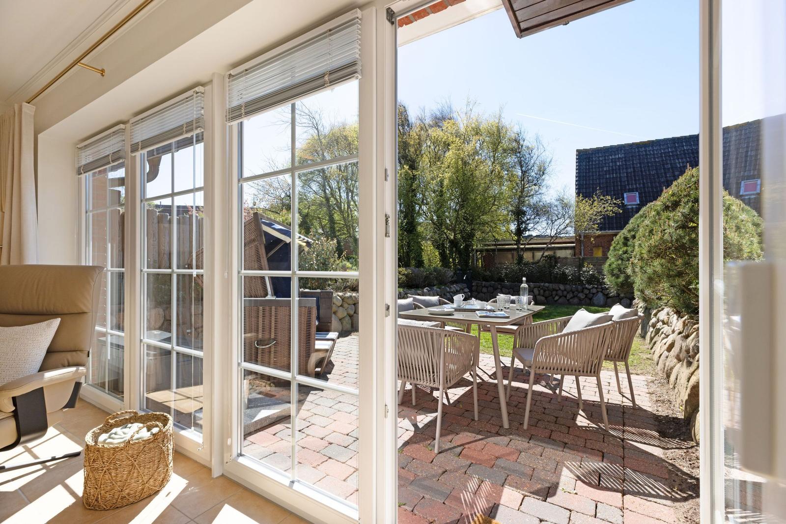 Durchgehende Glasschiebetüren führen auf eine Terrasse mit Tisch und Stühlen.