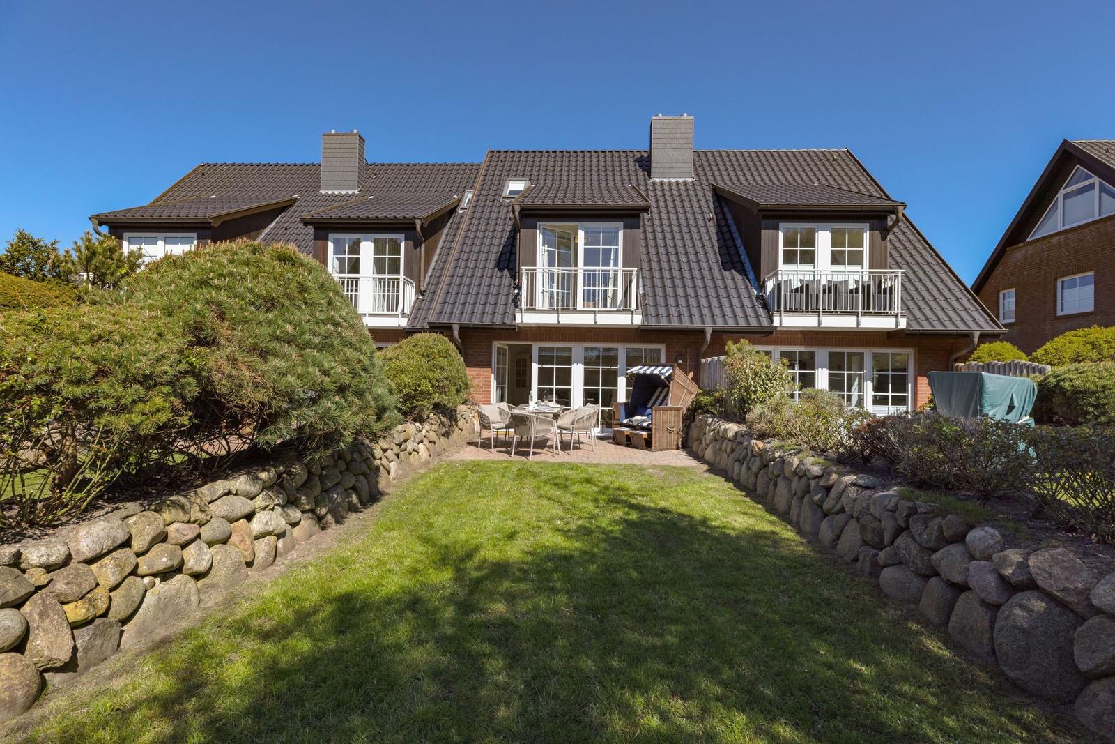 Haus mit Balkon, Terrasse und Garten. Steinmauern umgeben den Rasen.