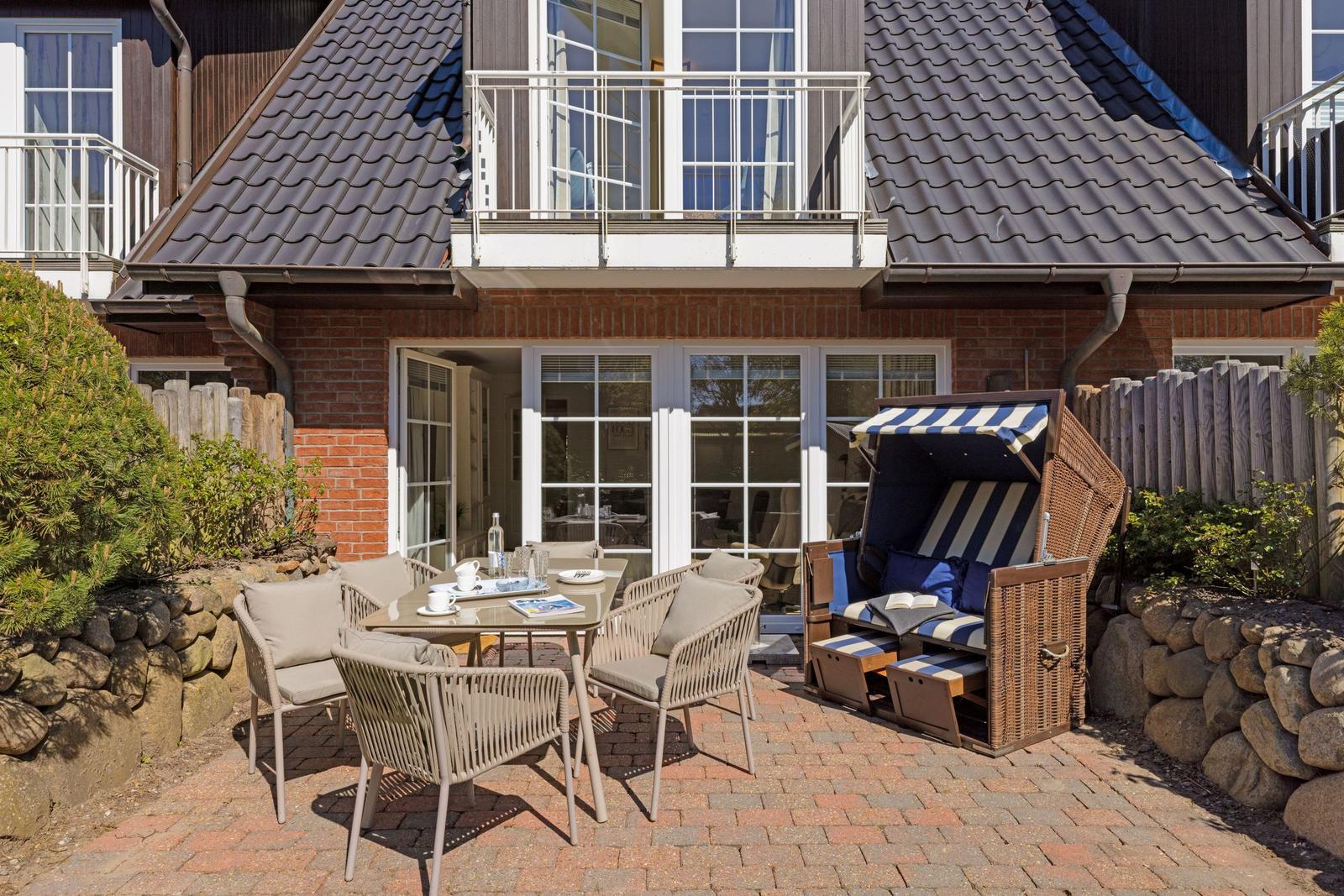 Terrasse mit Tisch, Stühlen und Strandkorb vor Haus mit Balkon.