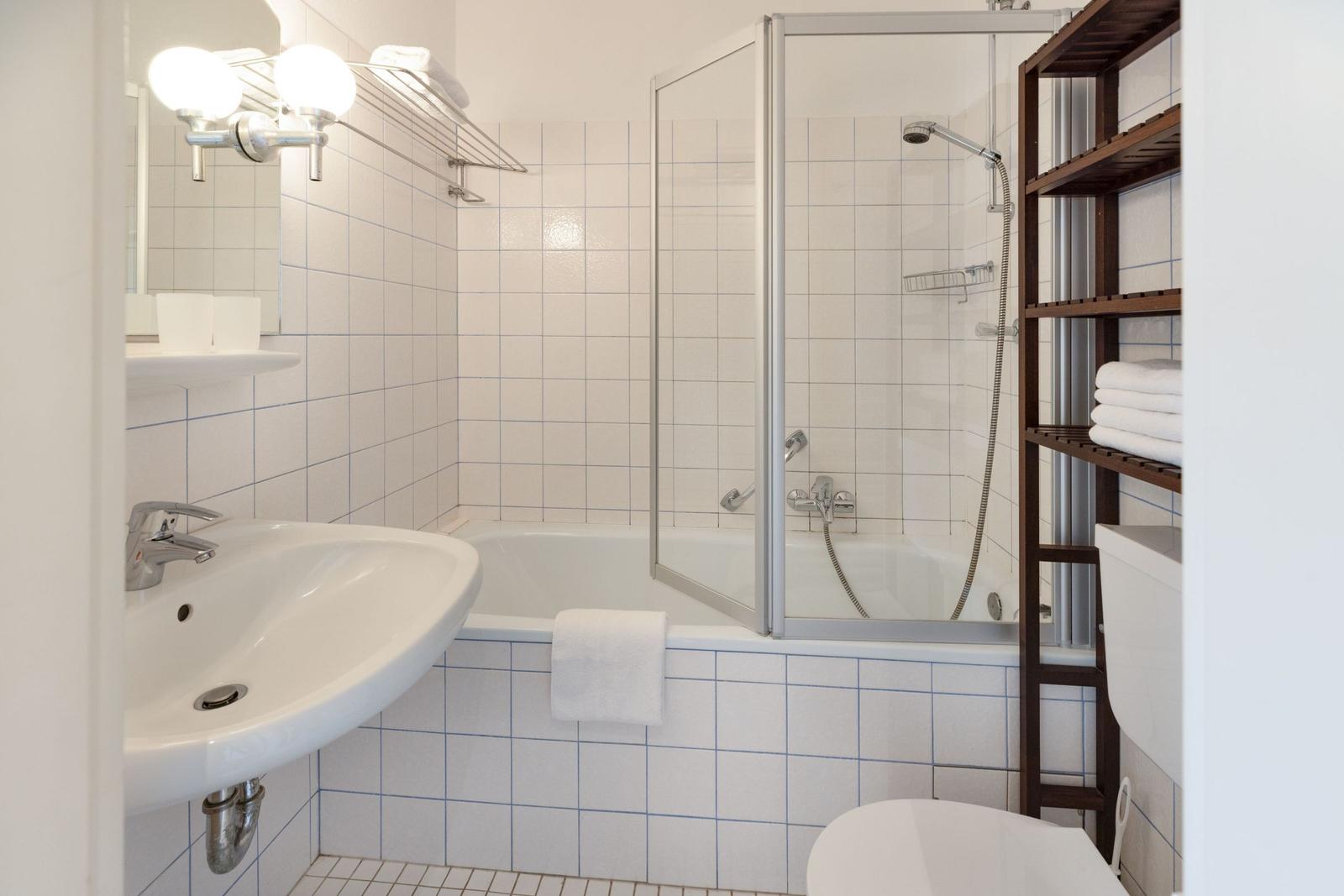 Badezimmer mit Badewanne, Dusche, Waschbecken und Holzregal.