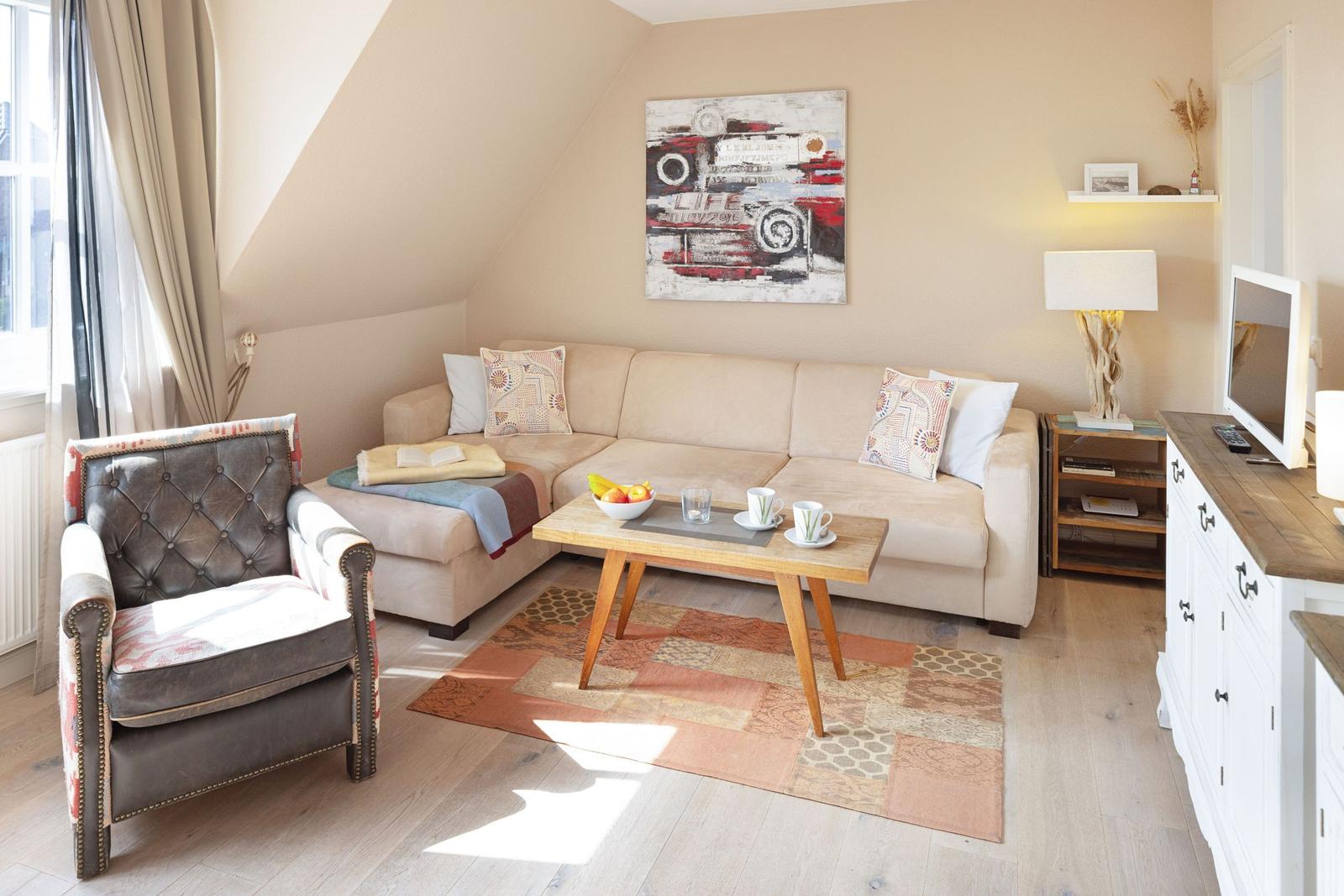 Wohnzimmer mit Sofa, Sessel, Couchtisch und Fernseher. Wandbild und Teppich sind sichtbar.